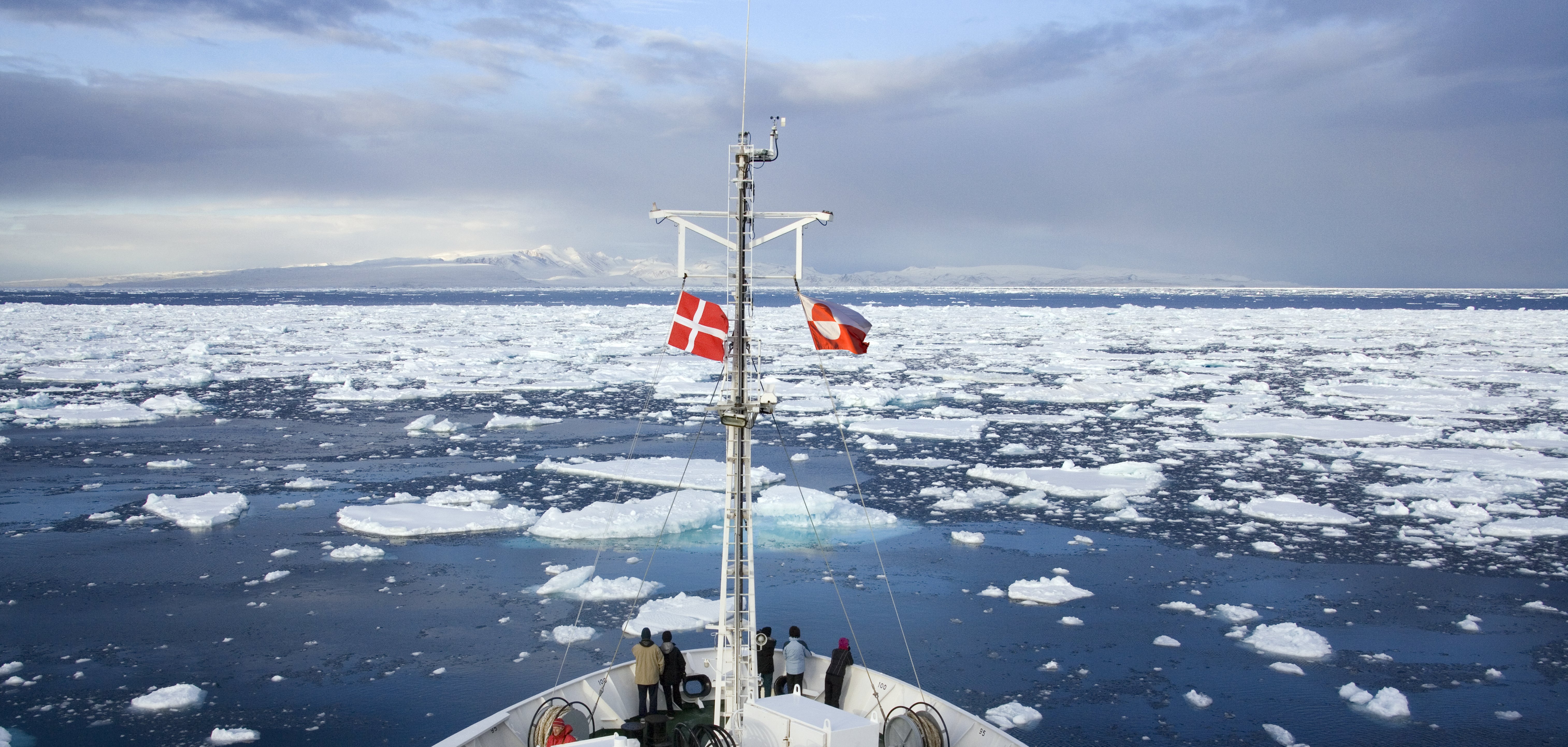 SKib der sejler gennem is. Skibet har henholdsvis dansk og grøndlansk flag på.